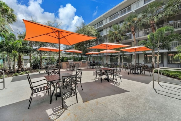 An outdoor patio area with tables and chairs, surrounded by palm trees and a building with balconies. - Spacious Apt Perfect for Disney (Kissimmee)