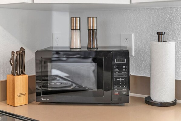 Een zwarte magnetron met digitaal display, twee kruidenhouders en een rol keukenpapier op een aanrecht.