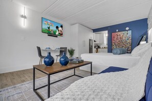 Ein modernes Wohnzimmer mit einem Flachbildfernseher, der 'Mickey Mouse Clubhouse' zeigt, einem Sofa, einem Couchtisch mit dekorativen Vasen sowie einem Essbereich mit Stühlen und einem kleinen Tisch.