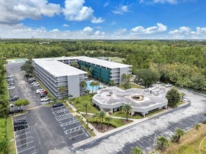 A multi-story hotel with a parking lot, a swimming pool, and a landscaped area with palm trees. - Lux King Suite 7 min Disney + Pool + Free Parking (Kissimmee)