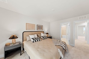 A bedroom with a bed, nightstands, a lamp, a picture frame, and a door leading to a bathroom. - 2 Lux Homes, Game Rooms, Pool, Bikes, 10 Balconies (Ocean City)