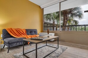 A modern living room with a sofa, a coffee table, and a view of palm trees through large windows. - Beauty Studio 7 min from Disney World & Universal (Kissimmee)