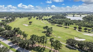 Un campo de golf con cielo despejado, árboles y una masa de agua a lo lejos.
