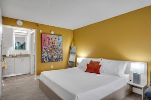 Ein Hotelzimmer mit Bett, Nachttisch, Fenster und sichtbarem Badezimmer durch eine geöffnete Tür.