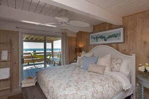 Ein Schlafzimmer mit Bett, Deckenventilator, Holzwand, gerahmtem Bild und Blick auf das Meer.
