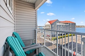 A balcony with teal chairs, a railing, and a view of a marina with boats and a building with a red roof. - 3 Spacious Dwntwn Condos Bay Views Steps to Boards (Ocean City)