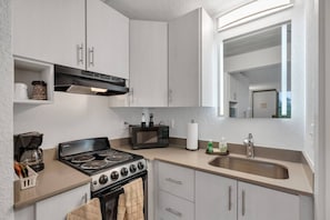 A compact kitchen with a stove, microwave, and sink, featuring white cabinetry and a window above the sink. - 7 min to Disney Luxury Blue King + Pool Parking (Kissimmee)