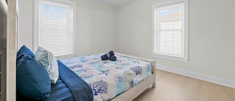A bedroom with a bed, two windows with blinds, a ceiling vent, and a wooden floor.