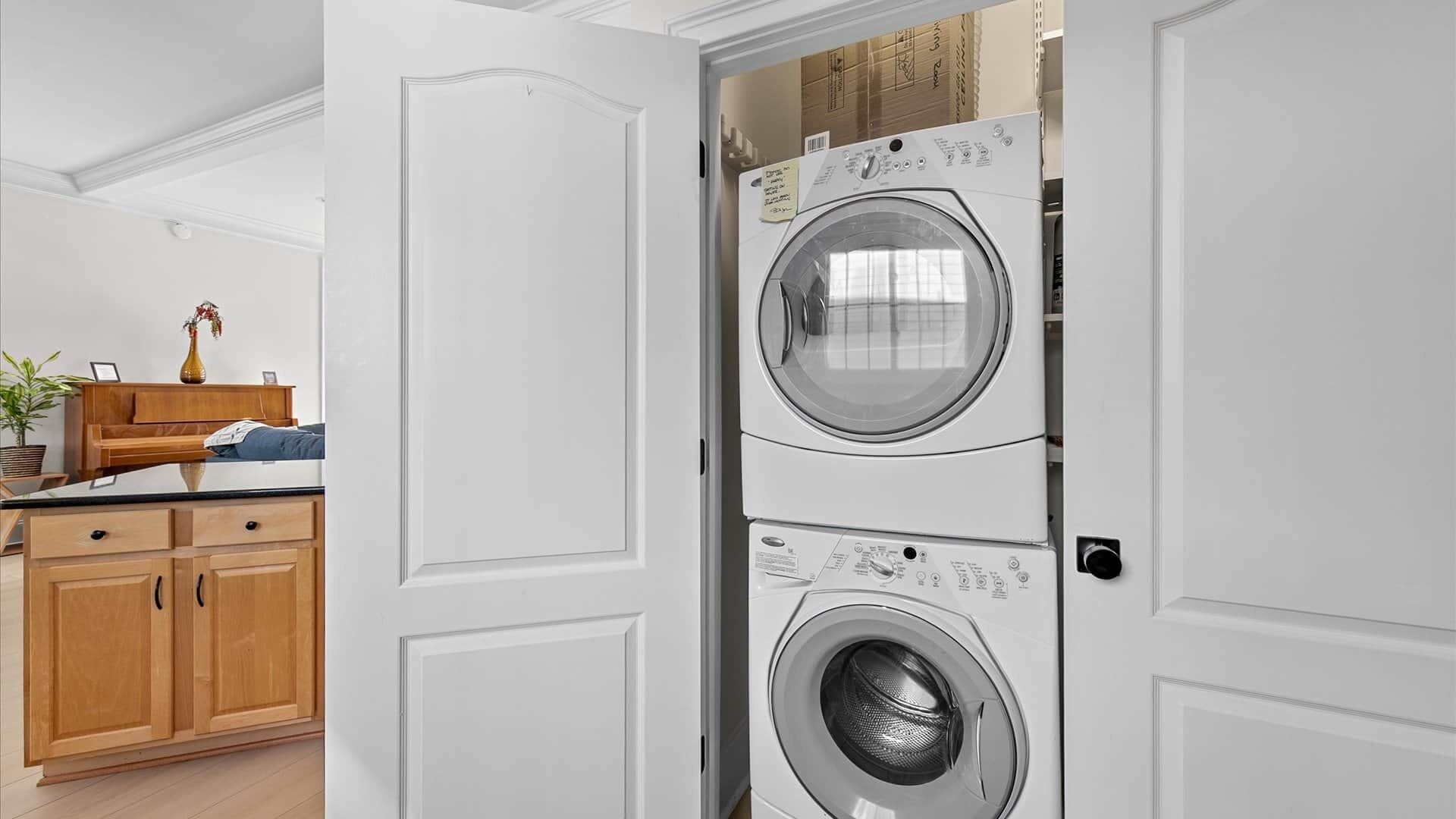 Une buanderie équipée de machines à laver et de sèche-linge superposés, de meubles en bois et d’une plante.
