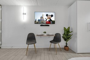 A modern room with a flat-screen TV displaying a cartoon character, two chairs, a small table with a plant, and a potted plant. - Chic Studio Near Disney World + Free Parking (Kissimmee)