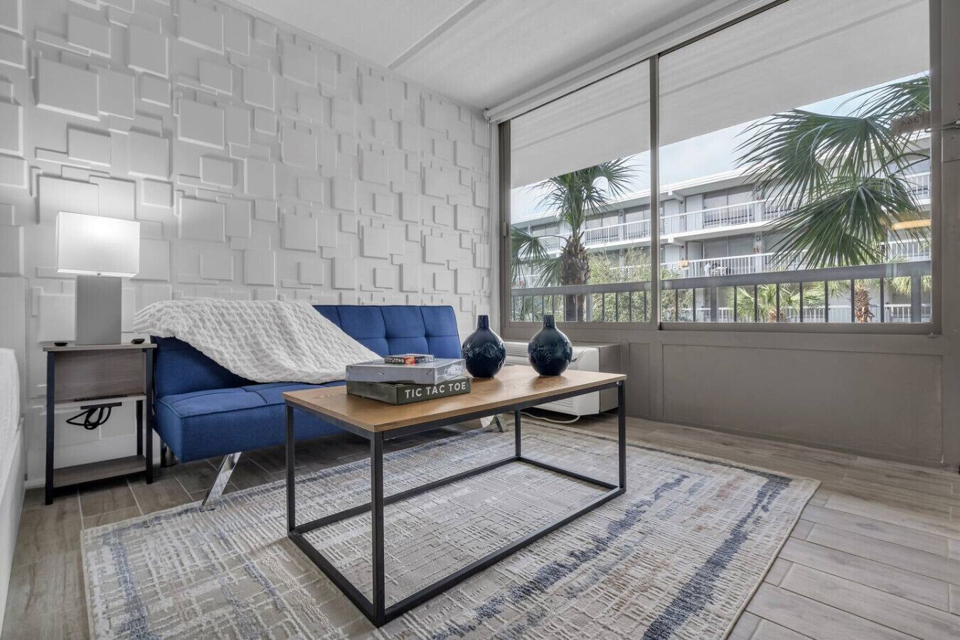 Ein modernes Wohnzimmer mit einem blauen Sofa, einem Holztisch und einem gemusterten Teppich.