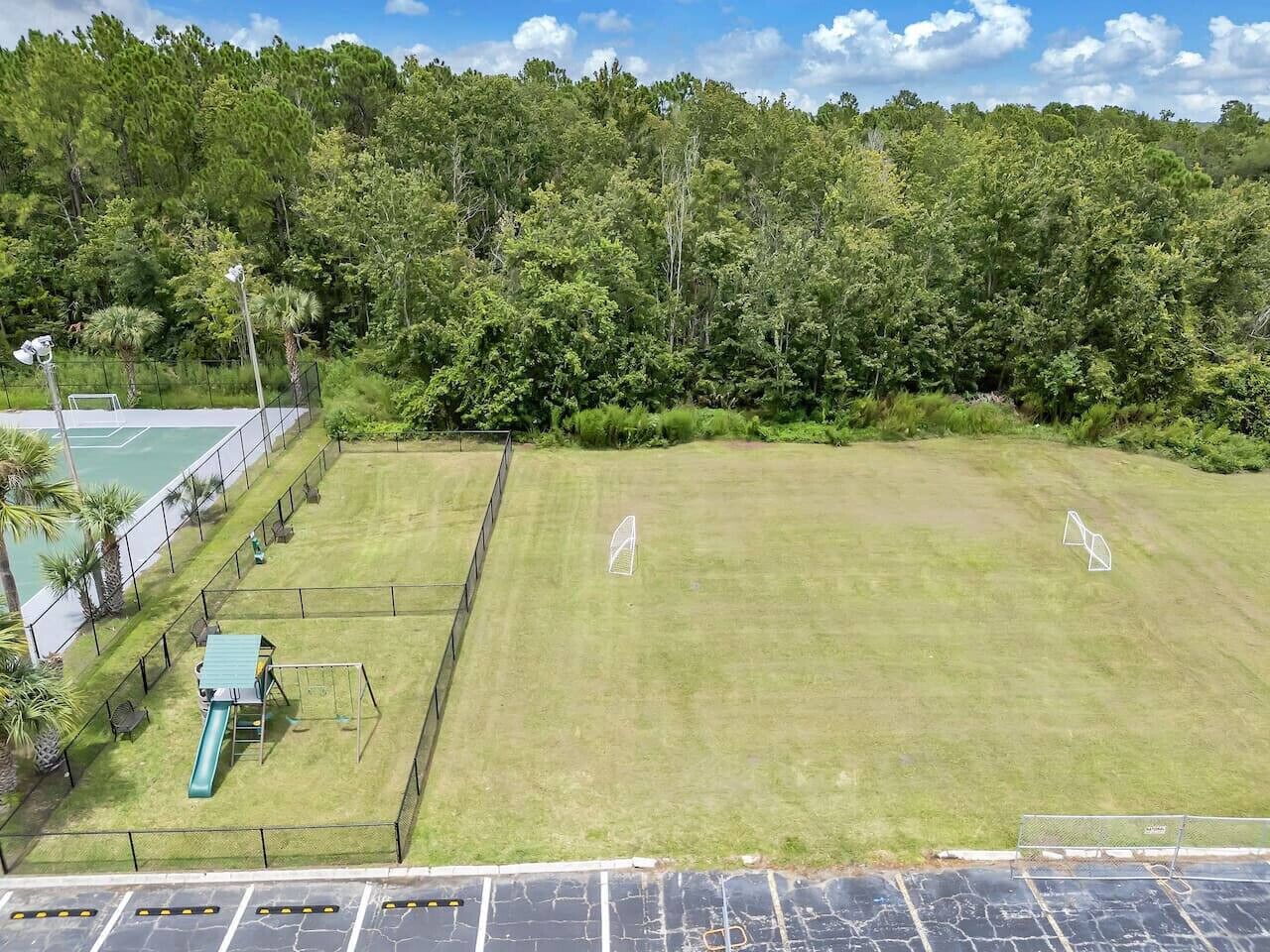 Zona exterior tancada amb àrea de jocs, una pista de tennis i un camp de gespa.