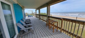 A wooden deck with a view of the ocean, a lounge chair, a table, and a small building in the background. - Beachfront House - Sunny Beach Retreat (Gilchrist)