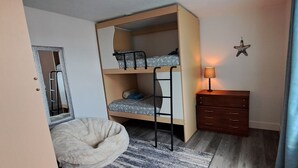 Una cama litera con escalera, un pequeño aparador de madera, una lámpara y una decoración con forma de estrella en la pared.