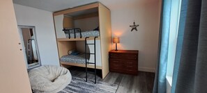 En køjeseng med stige, en lille trækommode, en lampe og en stjerneformet dekoration på væggen.