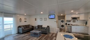 Ein Wohnzimmer mit Sofa, Couchtisch, Fernseher und einer Küchenzeile mit Geräte.