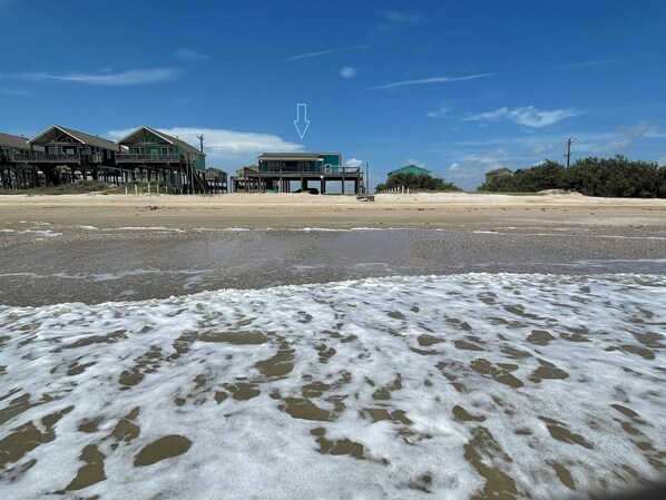 En ejendom ved stranden med flere bygninger, herunder en markant grøn bygning med balkon.