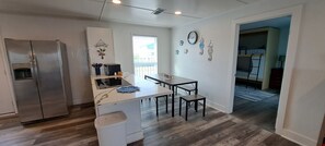 A compact kitchen with a refrigerator, a small dining area with a table and chairs, and a view of a balcony. - Beachfront House - Sunny Beach Retreat (Gilchrist)