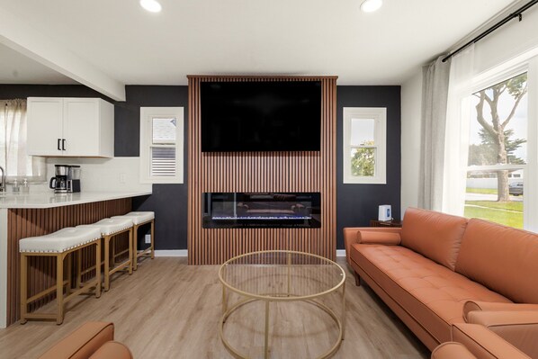Una sala de estar moderna con un sofá, una mesa de centro, un televisor y un área de cocina con cafetera.