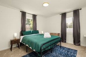 Un lit simple avec une couvre-lit verte, une table de chevet avec une lampe et un tapis bleu à motifs.