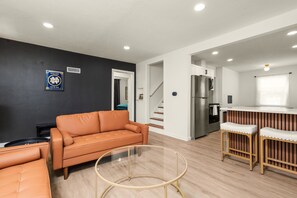 Ein modernes Wohnzimmer mit einer Couch, einem Glastisch und einer Küchenzeile mit Kühlschrank und Barhocker.