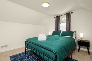 Un dormitorio con cama, mesita de noche, ventana con cortinas y lámpara en el techo.