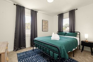 Un dormitorio con cama, mesita de noche, lámpara y ventana con cortinas.