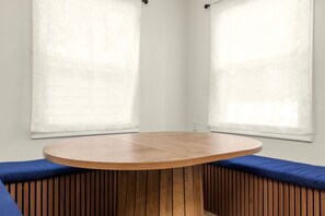 A round wooden table with a blue cushioned bench in front. - Rockne Retreat<>6BR 3BA Home Close to ND (South Bend)