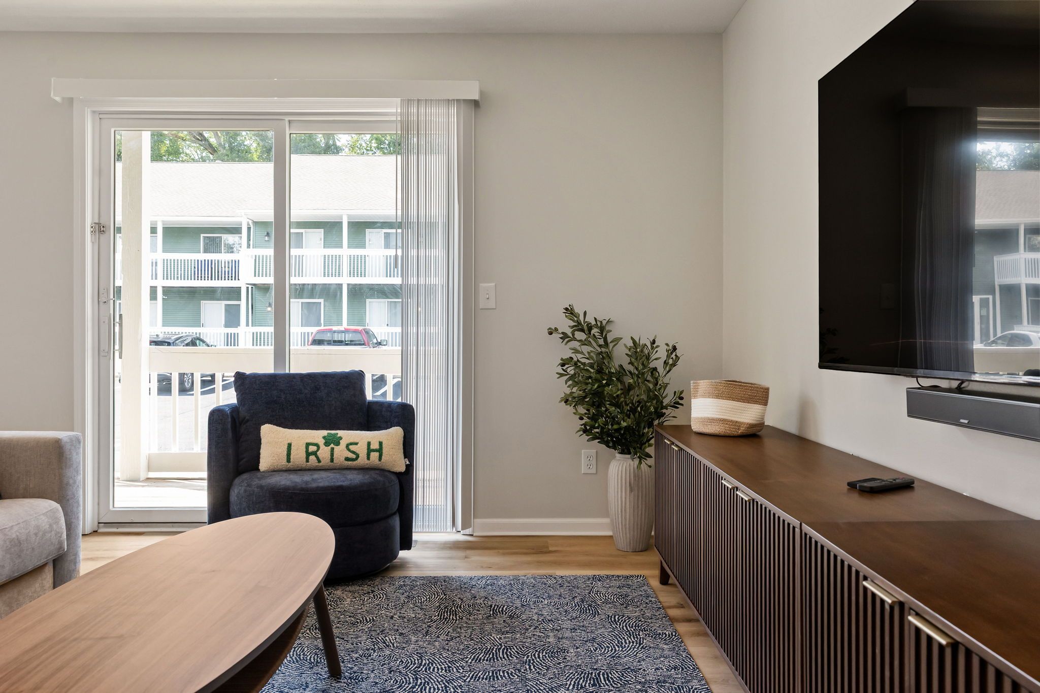 A modern living room with a sofa, a coffee table, a TV, and a sliding glass door leading to a balcony.