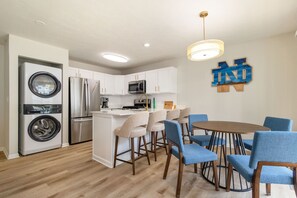 A modern kitchen with stainless steel appliances, a dining area with blue chairs, and a wall-mounted artwork.