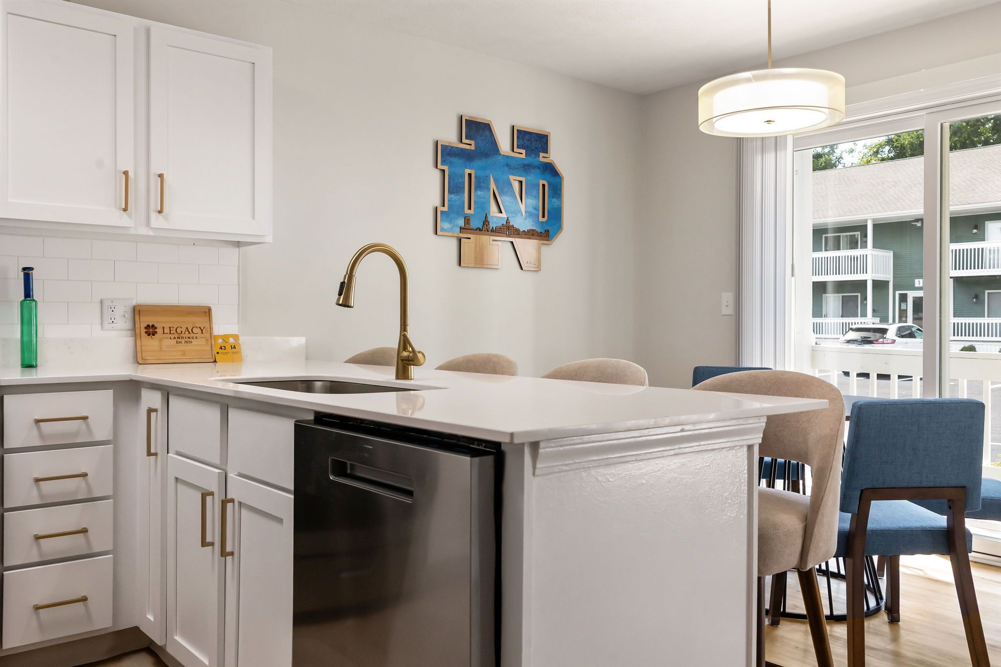 A modern kitchen with white cabinetry, a stainless steel dishwasher, and a pendant light.