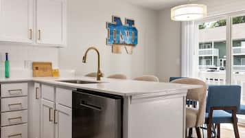 A modern kitchen with white cabinetry, a stainless steel dishwasher, and a pendant light.