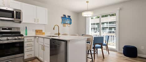 A modern kitchen with stainless steel appliances, a central island, and a dining area with chairs.