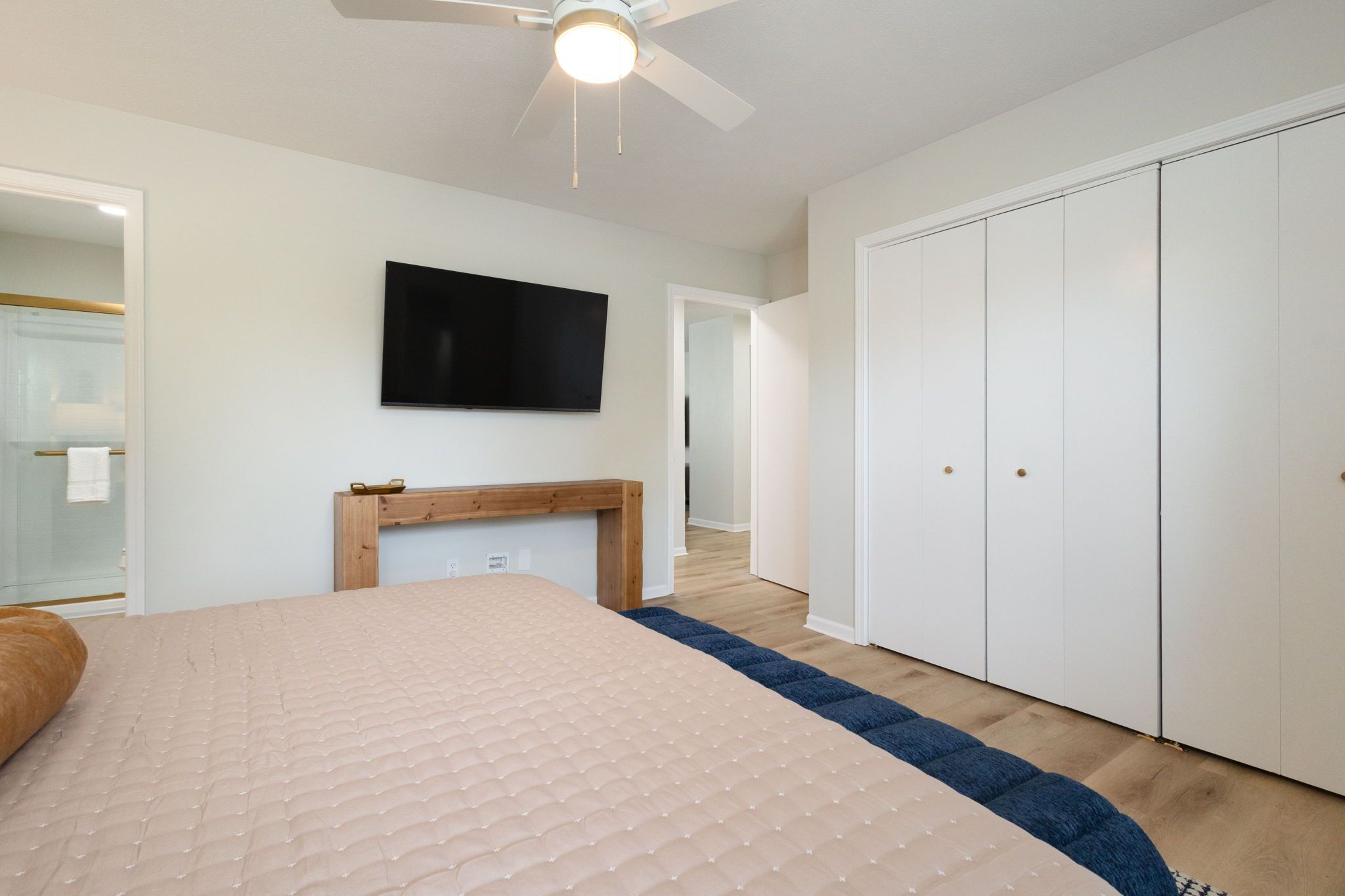 A bedroom with a bed, a television, a wardrobe, and a ceiling fan.