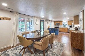 Uma sala de jantar espaçosa com uma mesa redonda e cadeiras, cozinha ao fundo, e vista pela janela.