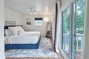 Quarto com cama, ventoinha no teto, janela com cortinas e vista para o verde lá fora.