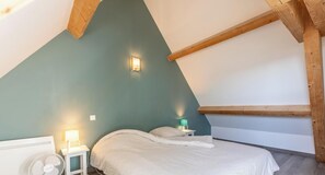 Une chambre avec un plafond en pente, un lit avec une literie blanche, une table de chevet avec une lampe et un luminaire fixé au mur.