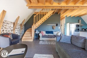 A modern living room with a curved staircase, a stone wall, and a kitchen area. - The Sancy - SAINT SAUVES D'AUVERGNE (SAINT SAUVES D'AUVERGNE)