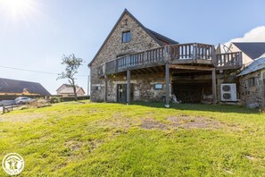 Un bâtiment en pierre doté d’un balcon, d’une entrée couverte et d’une cour gazonnée.