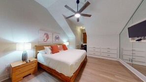 A bedroom with a sloped ceiling, a bed with white bedding, a wooden nightstand, a desk, and a wardrobe. - Hooked on Baytowne | Fisherman’s Village | 2 King Suites + Resort Tram (Miramar Beach)