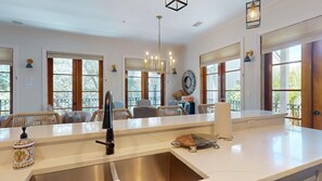 Una habitación amplia con un gran ventanal, una araña de cristal y un comedor con mobiliario de mimbre.