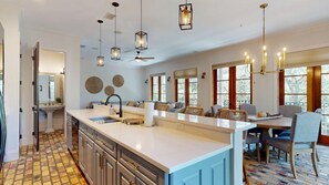 A spacious kitchen with a large island, modern pendant lighting, and a dining area with a view. - Hooked on Baytowne | Fisherman’s Village | 2 King Suites + Resort Tram (Miramar Beach)