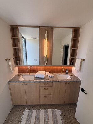 Uma casa de banho moderna com lavatório duplo, armários de madeira e um espelho grande.