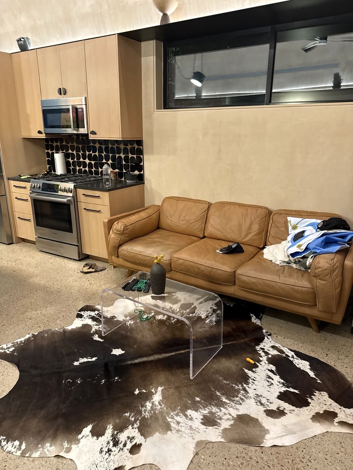 A living room with a brown leather sofa, a glass coffee table, and a cowhide rug.