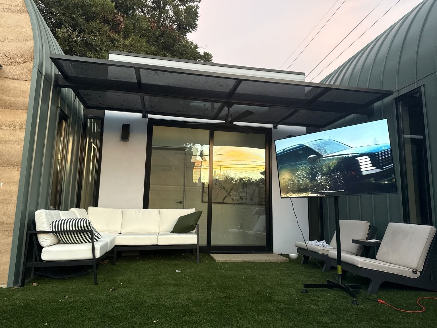 Ein moderner Außenbereich mit Glastür zu einer Terrasse, einem weißen Sofa, einem flachbildschirmfernseher an der Wand und einem Deckenventilator.