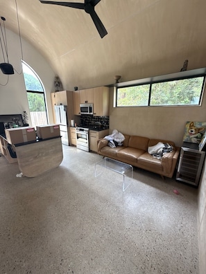 Uma sala de estar ampla com cozinha compacta, sofá e ventilador de teto.