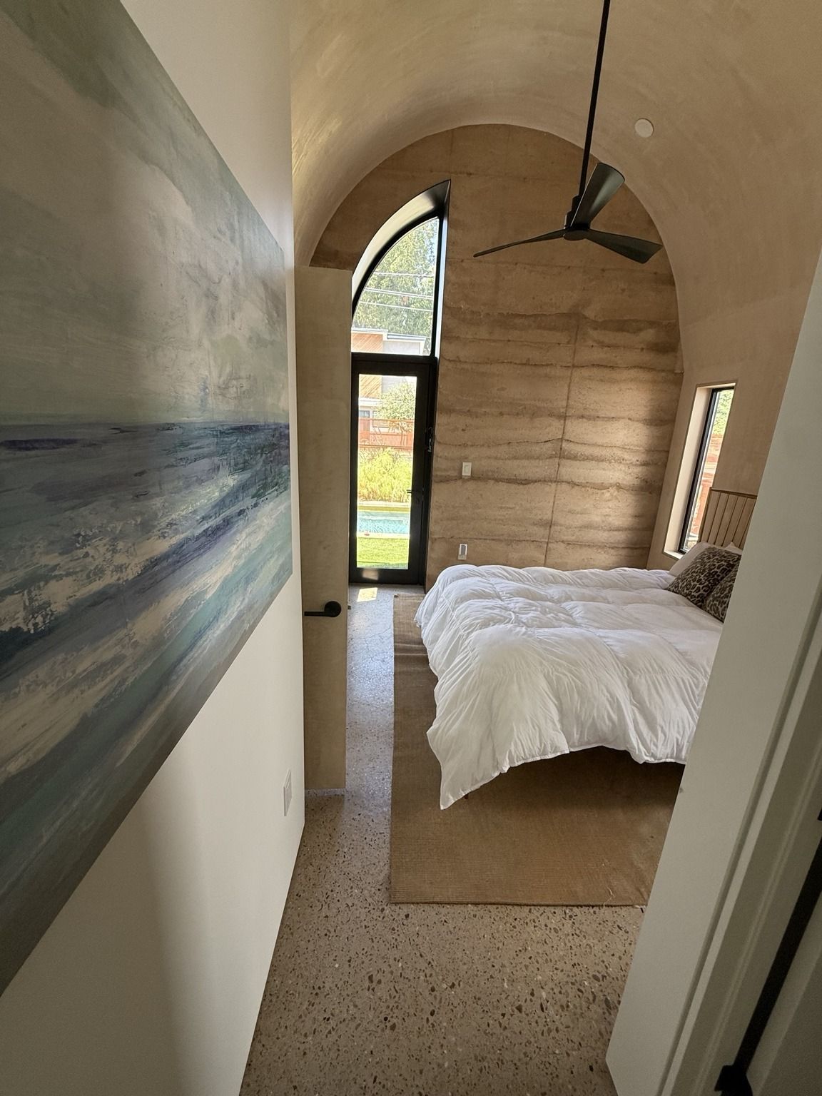 A bedroom with a bed, a ceiling fan, and a view of the outdoors through a window.