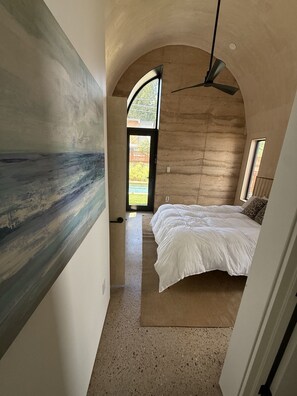 Quarto com cama, ventilador de teto e vista para o exterior pela janela.