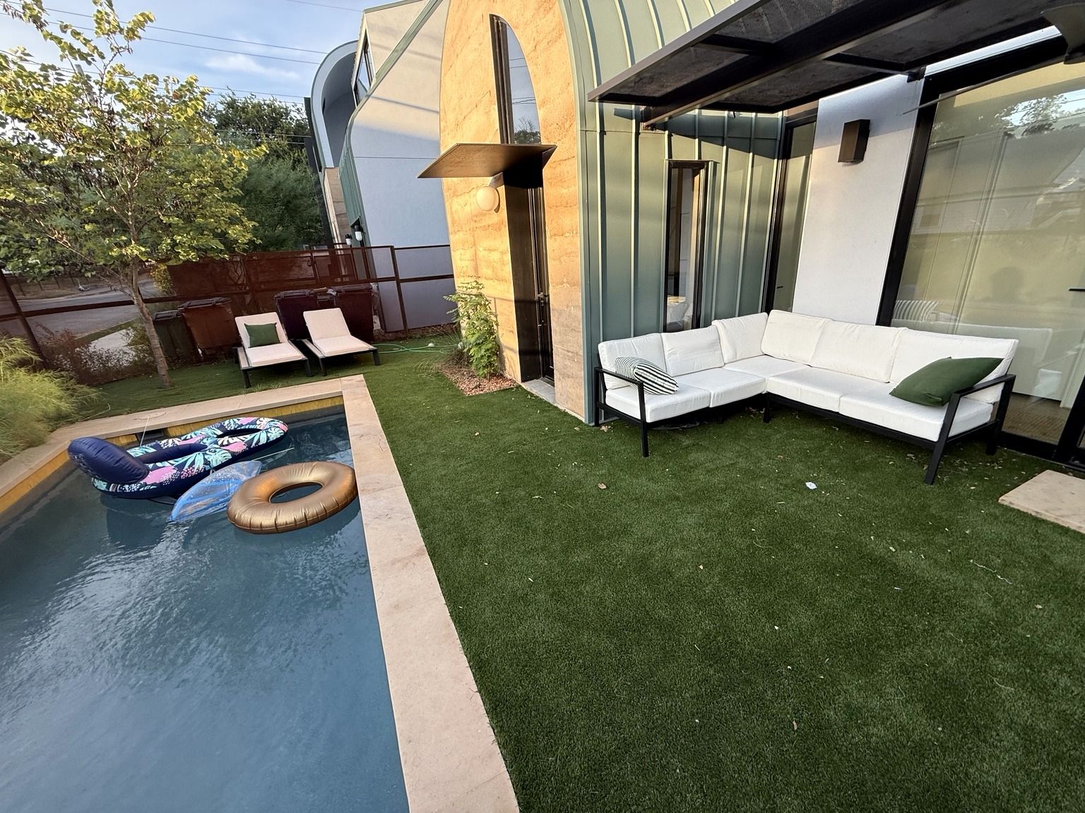 Ein moderner Außenbereich mit Pool, Rasenmatte, einem weißen Sofa und Lounge-Stühlen.
