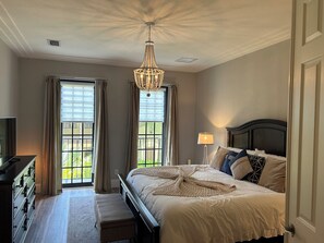 A bedroom with a bed, bedside lamp, and a chandelier. - OLE’ Lely resort. Beautiful 3-bedroom 2.5 bath townhome. Resort-style living! (Naples)